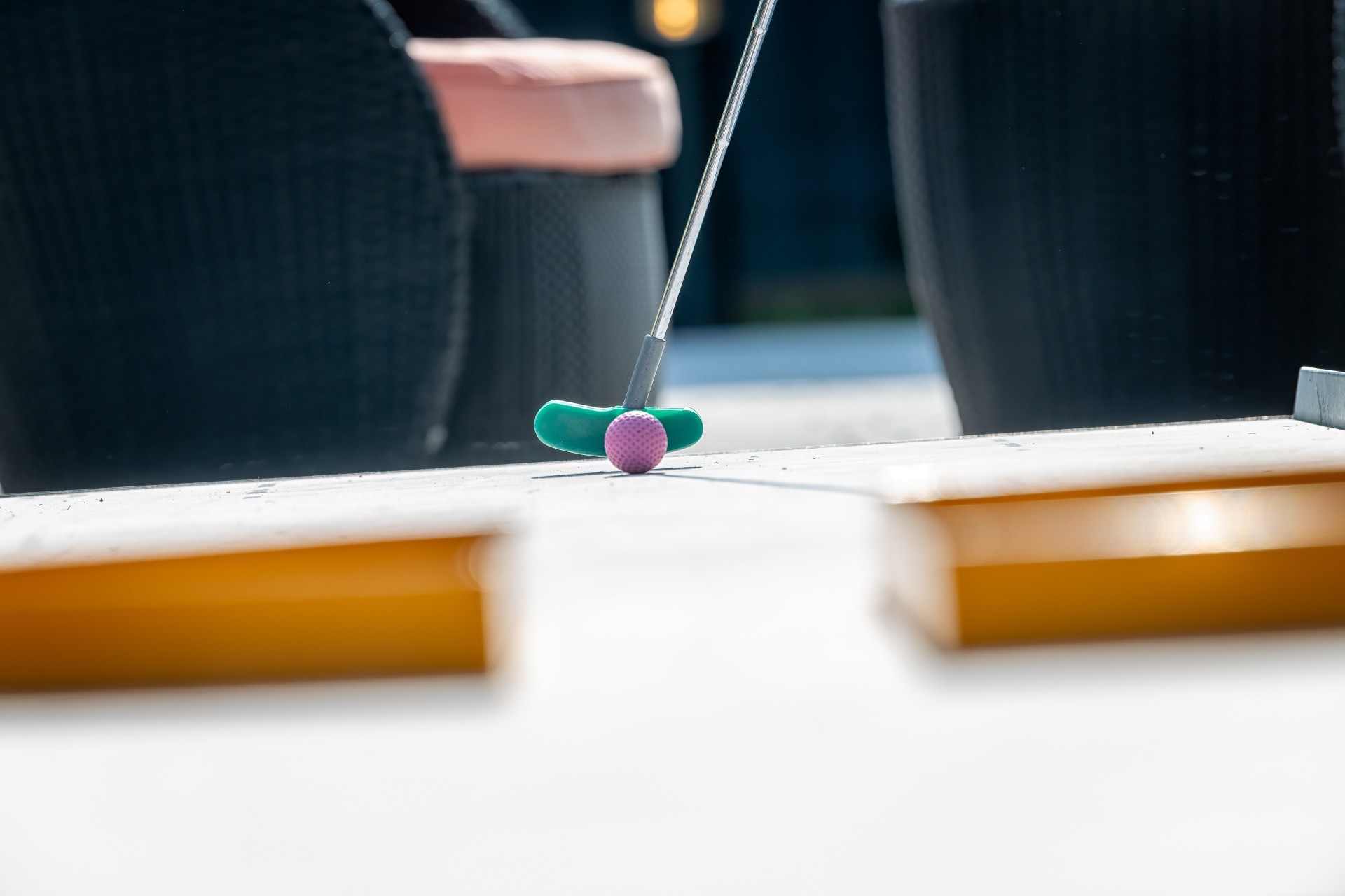 Mini golf club hitting a pink ball on the lane